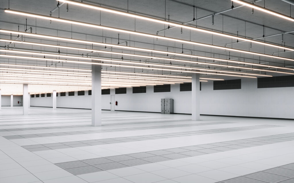Large data center interior with rows of server equipment, raised flooring, and overhead ceiling infrastructure